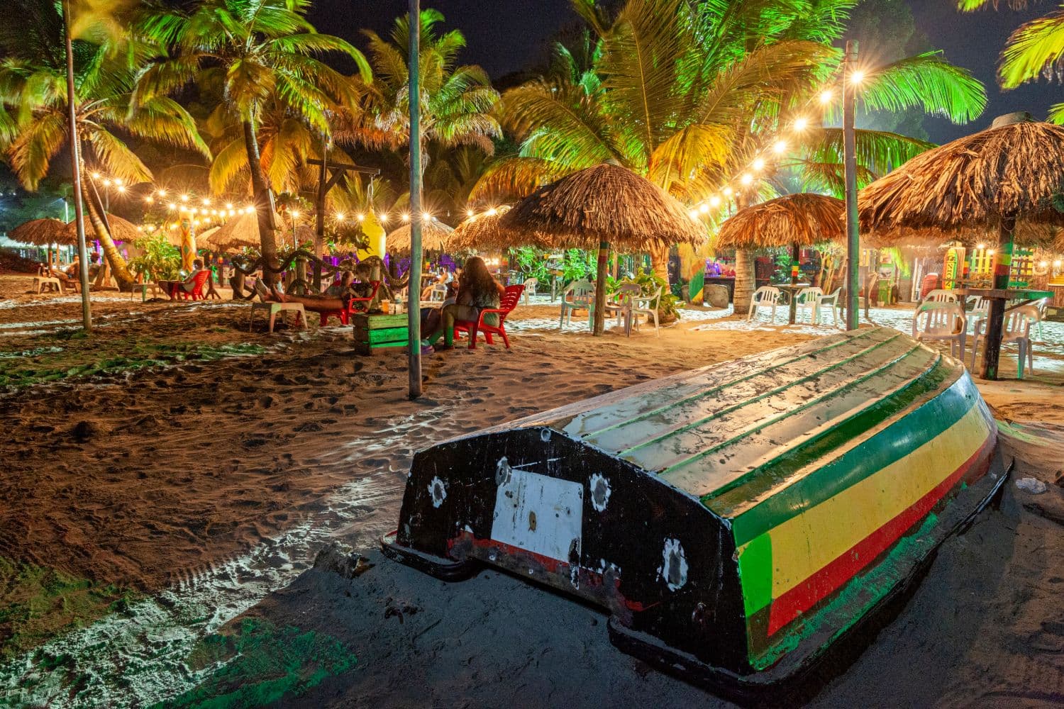 Playa de Necoclí de noche, con un bote tradicional pintado en verde, amarillo y rojo y palapas iluminadas